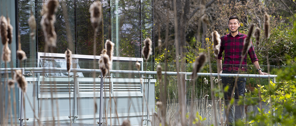 Student standing on the walkway over the pond outside the First Peoples House on the UVic campus.