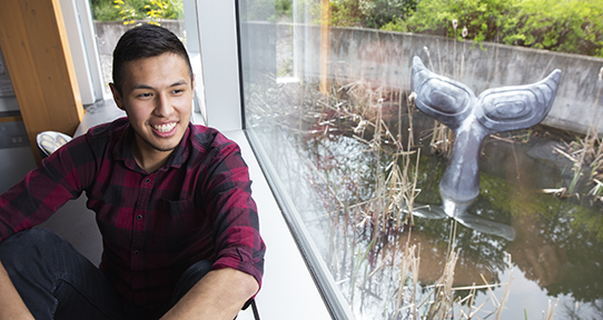 Student sitting in front of a window in First Peoples House looking at pond