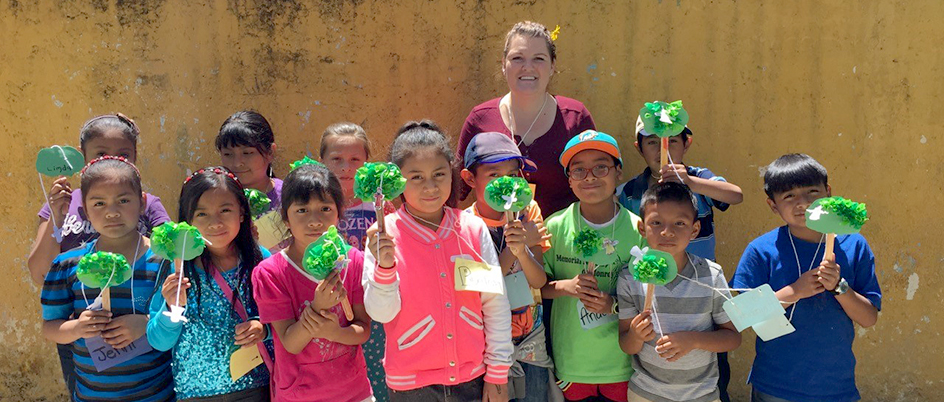 Female student standing with a group of children holding paper trees