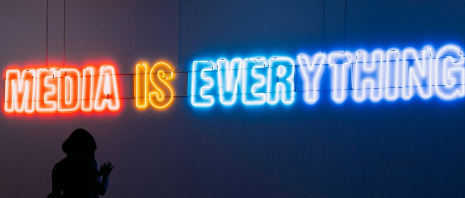 people look at a neon sign that says, "media is everything"