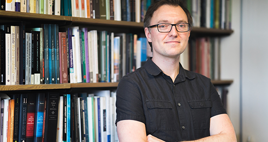 Dr. Mike Raven in front of bookshelf