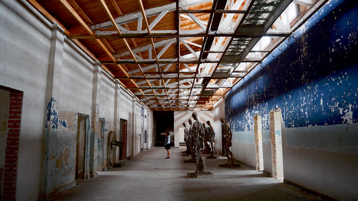 A student explores an exhibit of steel statues in a long hallway with exposed beams at Ravensbruck.