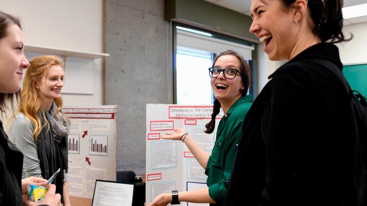 Linguistics students share their research at a poster fair in a brightly lit room with concrete walls.