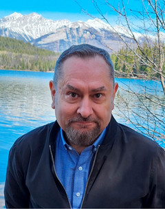 Profile photo of Serhy Yekelchyk standing outside in front of a body of water and a mountain landscape. 