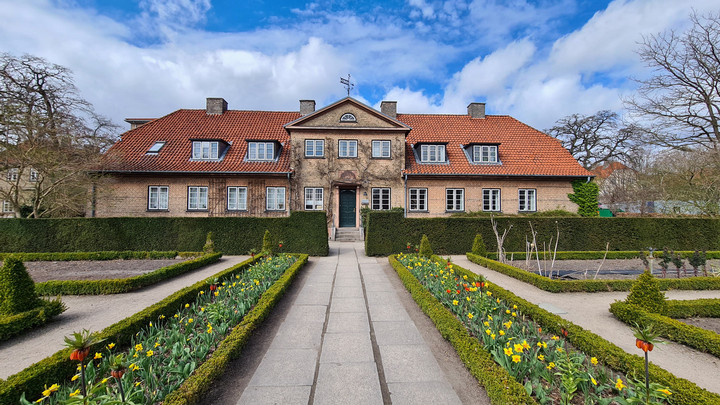 Frederiksberg Campus behind a flower garden and trimmed hedge.