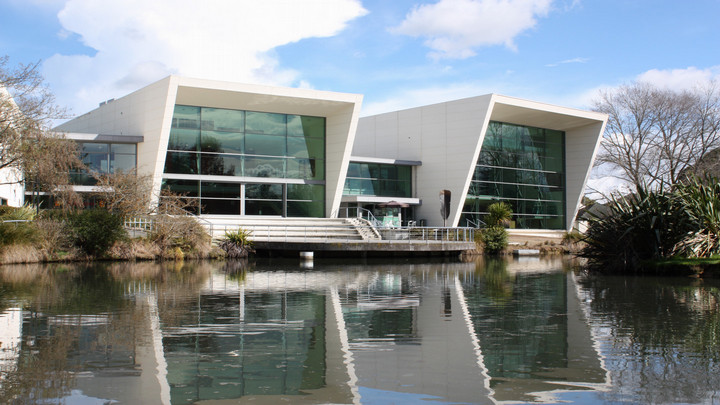 University of Waikato campus building surrounded by trees and bordering a pond.