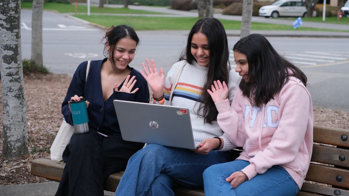 three UVic students wave use a laptop to connect with friends online