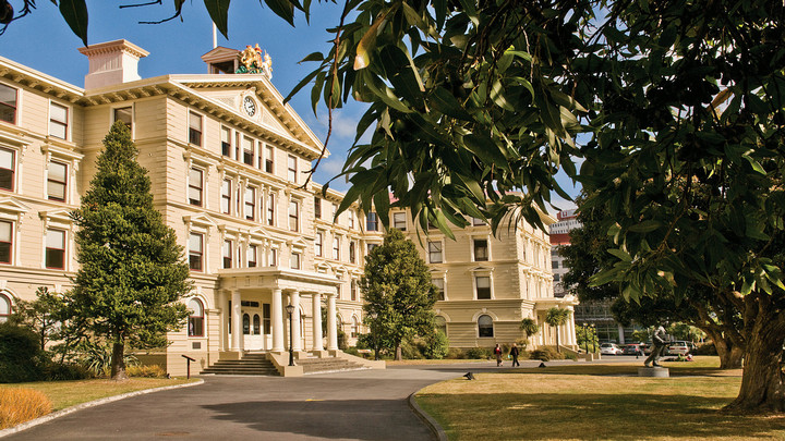 Two students walk in front of Victoria University Wellington Pipitea campus law school surrounded by trees