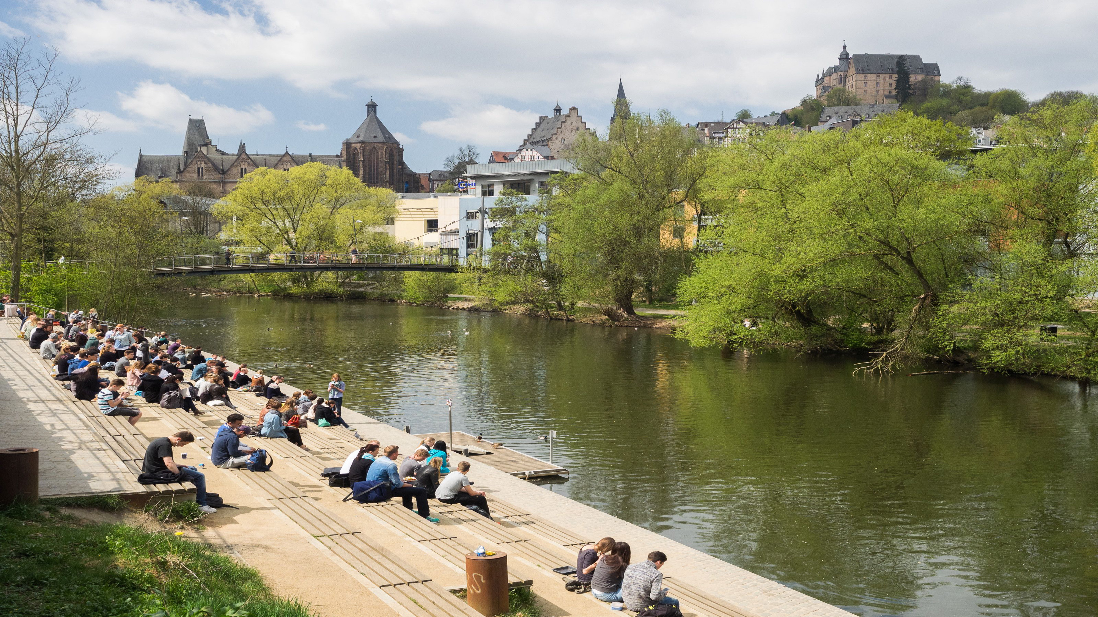 students sitting by the riverside at Marburg campus
