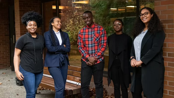 Five students stand in a row outside a building.
