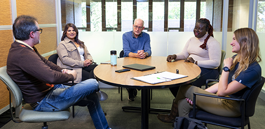 A group of people sit around a small, round table talking.