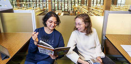 Two students sit together discussing a book