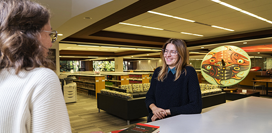 Two graduate students stand talking at the front desk of the law library