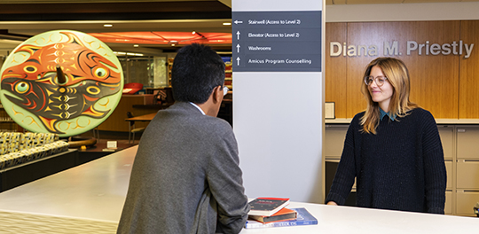 A student talks to a librarian behind the front desk of the library