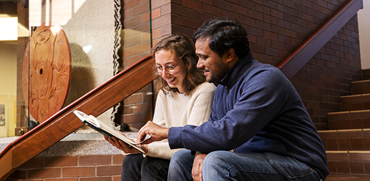 Two students sit on the stairs of the law building lobby.