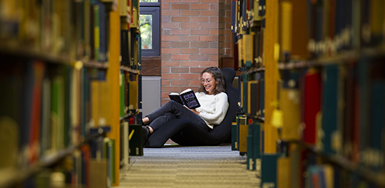 A student sits at the end of a long row of library shelves
