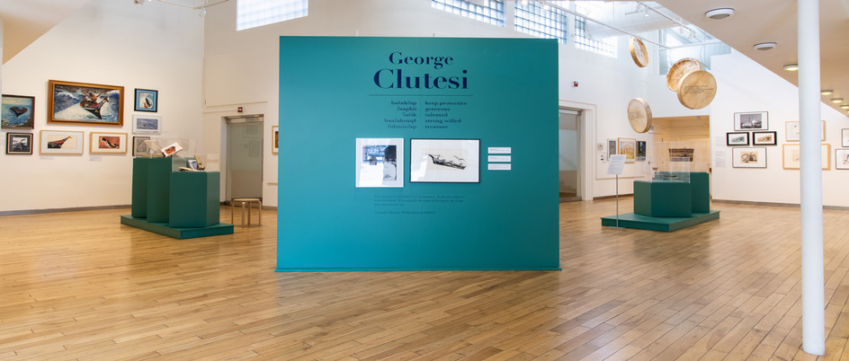 Wide view of the main gallery space for George Clutesi's exhibit. Paintings are visible on the walls in the background. 