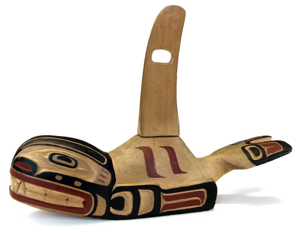 Wood carving in the shape of a killer whale by Henry Hunt. Black and red linework fill in the shape of a face, teeth, and fins.