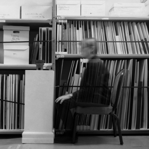 Artist sits facing a sculpture on a plinth in storage room