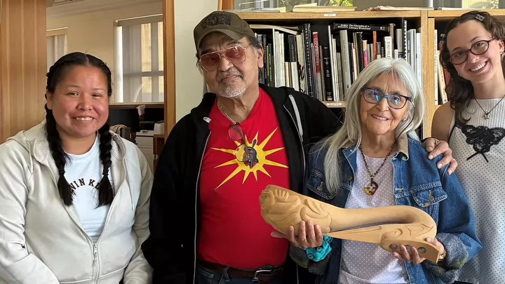 Four people standing together with one person holding a wood sculpture.