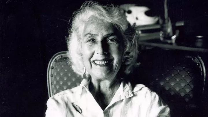 Edith has white hair and is wearing a white top and sitting in a chair.