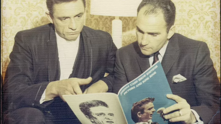 Two men sitting looking at a publication (Johnny Cash and Saul Holiff)