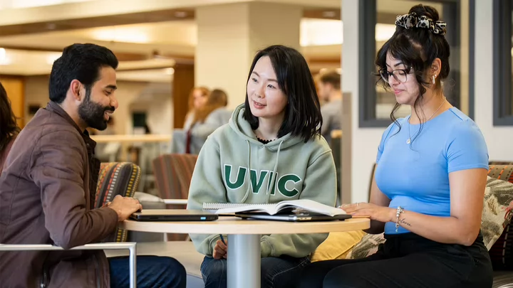 Three students sitting around a table in a library lounge.