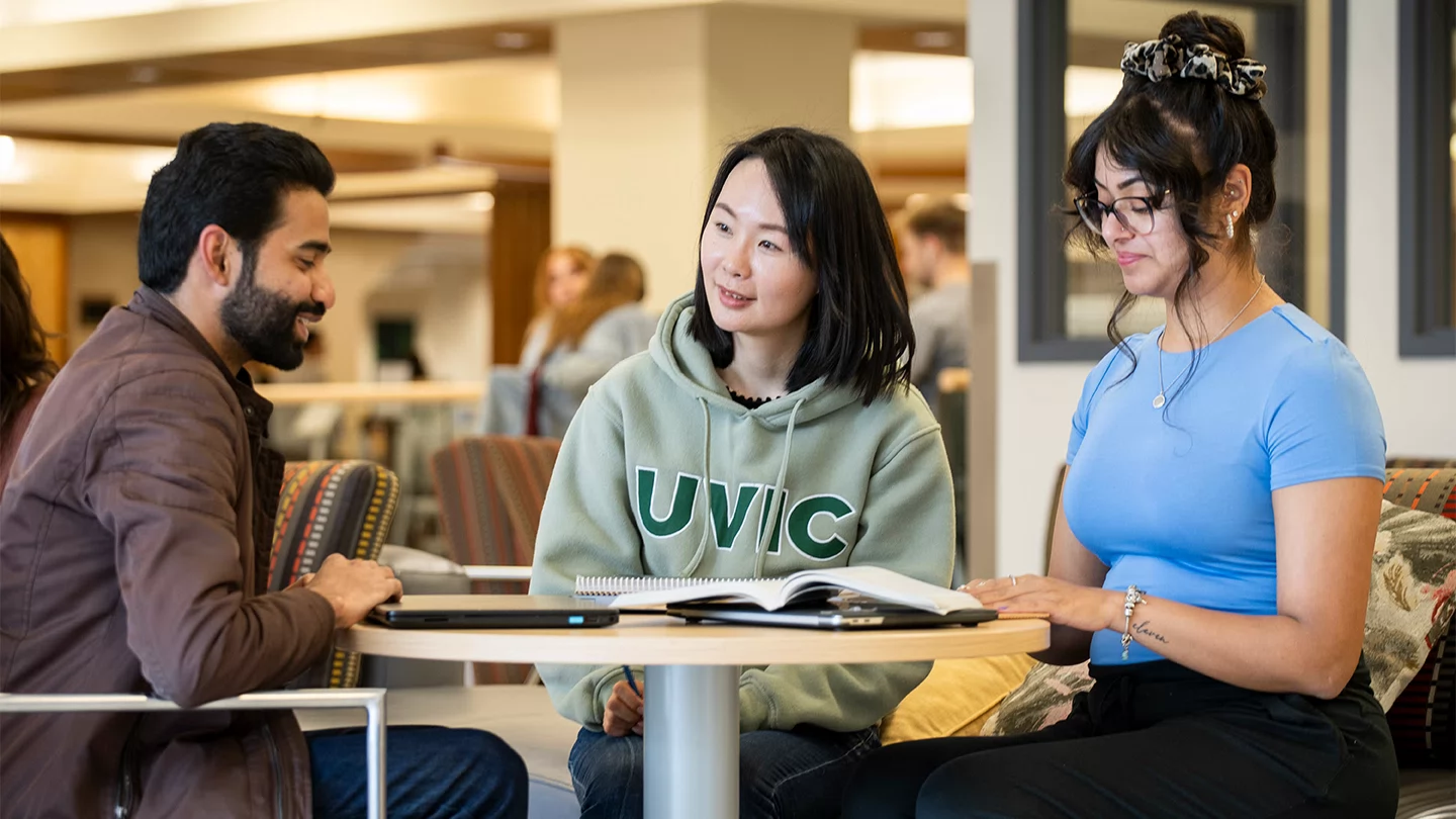 Three students sitting around a table in a library lounge.