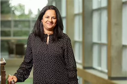Aditi is wearing a black and white spotted top standing in a library.