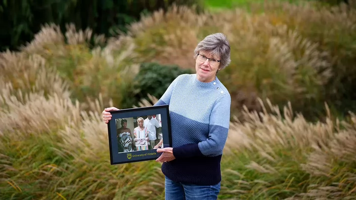Ann standing in tall grass holding a framed photo.