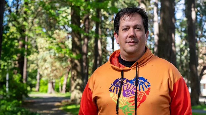 Carey standing in the forest wearing an orange hoodie.