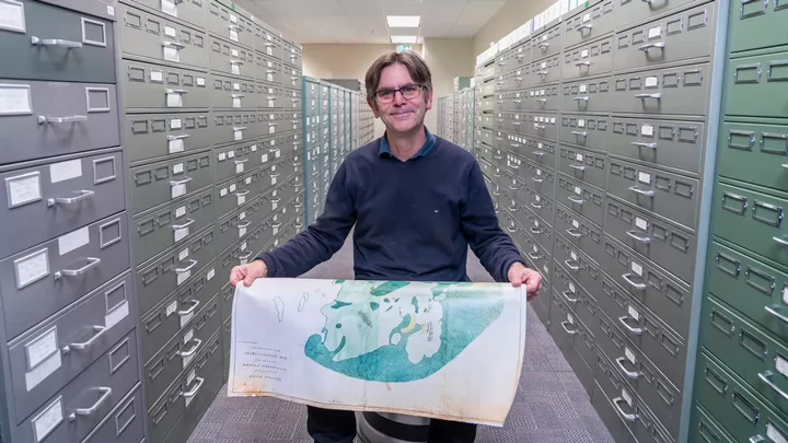 John in a row of filing cabinets holding a map.