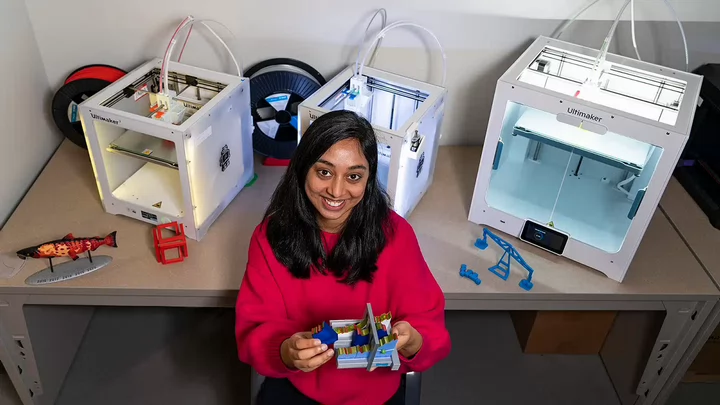 Somya sitting in front of three 3D printers.