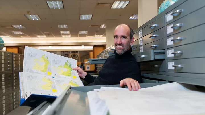 Tom sitting in front of an open map drawer holding a map.