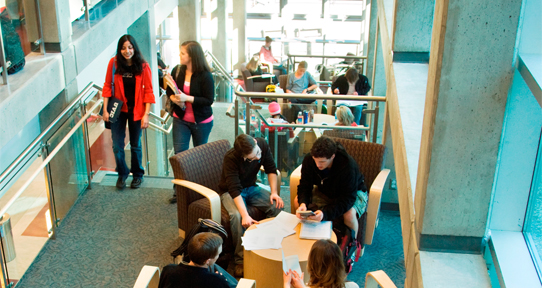 Students sitting around a table and working; two students walking up the stairs nearby.
