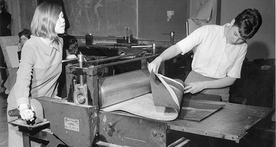 Two students using a printing press in an art studio.