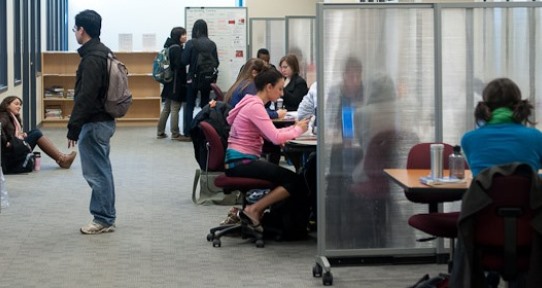Multiple students study alone or in small groups in the Learning Commons corridor.