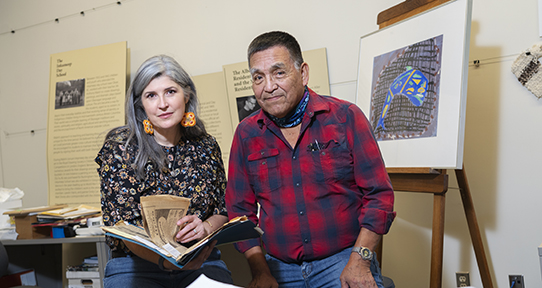 Andrea and Mark sitting on stools in front of framed artwork in a creative lab