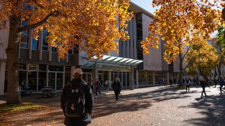 Student walking to the entrance of the Mearns Library on a fall day