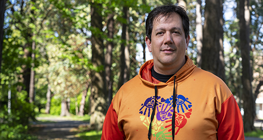 Carey standing in front of trees wearing an orange shirt