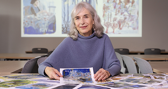 Charlotte sitting with colourful pages on a table from a soon-to-be-published graphic novel
