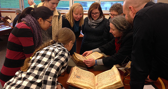 People gather around a medieval manuscript in the Special Collections reading room.