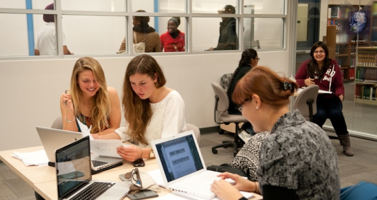 A small group of students chatting together as they work around a small table.