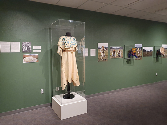 Exhibit displaying art in multiple media, including a dress, photographs, and animal masks
