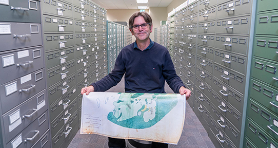 John sitting on a stool in the microfilm section holding a map