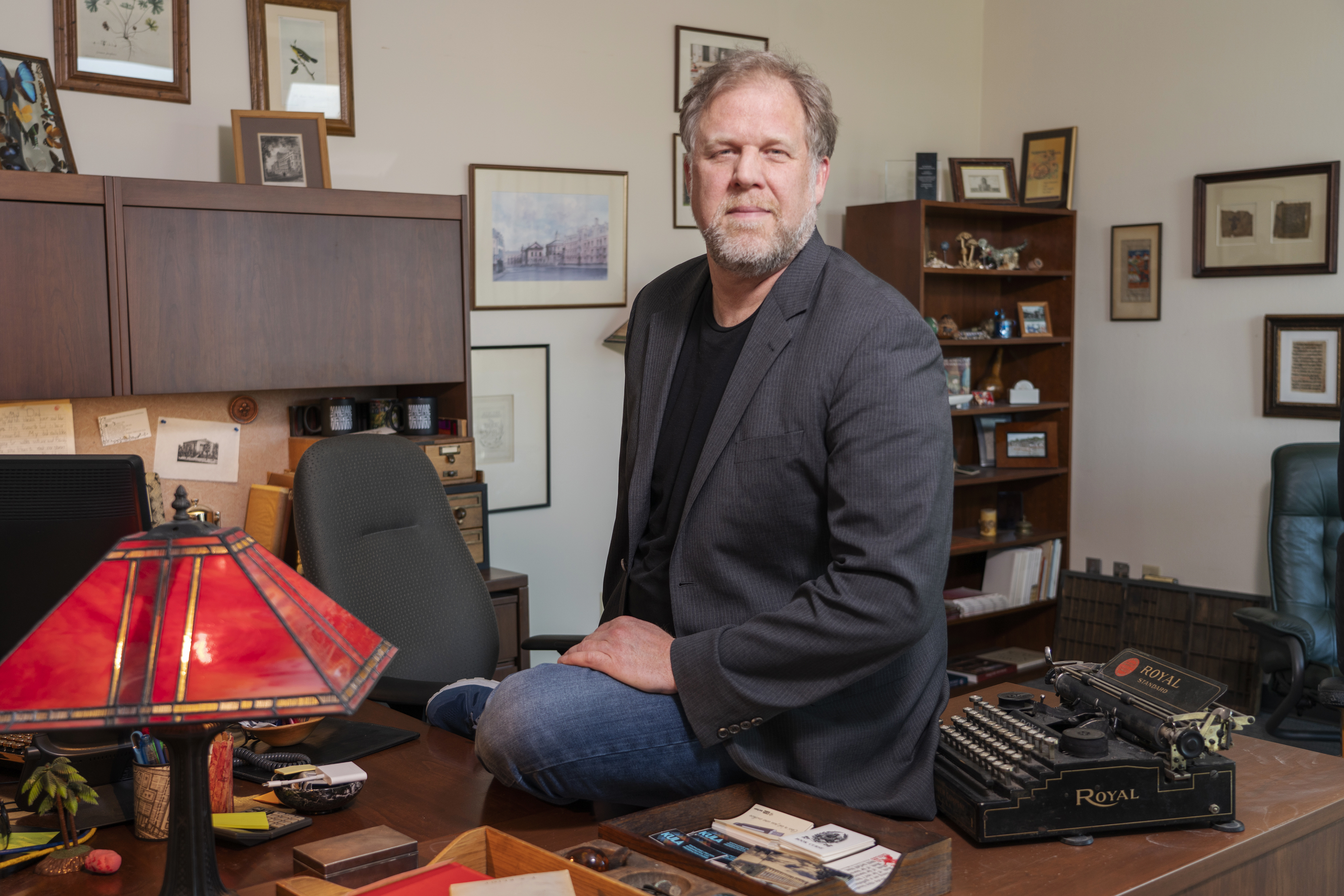 Jonathan Bengtson sitting on his desk next to a vintage typewriter in his office.