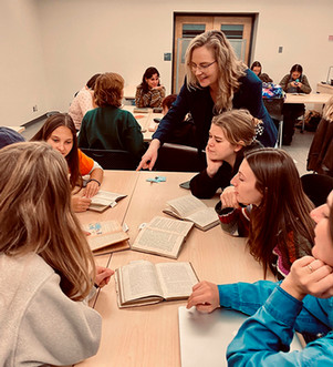 Teacher speaking with a group of students sitting around a table with textbooks