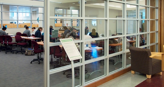 A classroom inside the library with glass walls and benches where students work together.