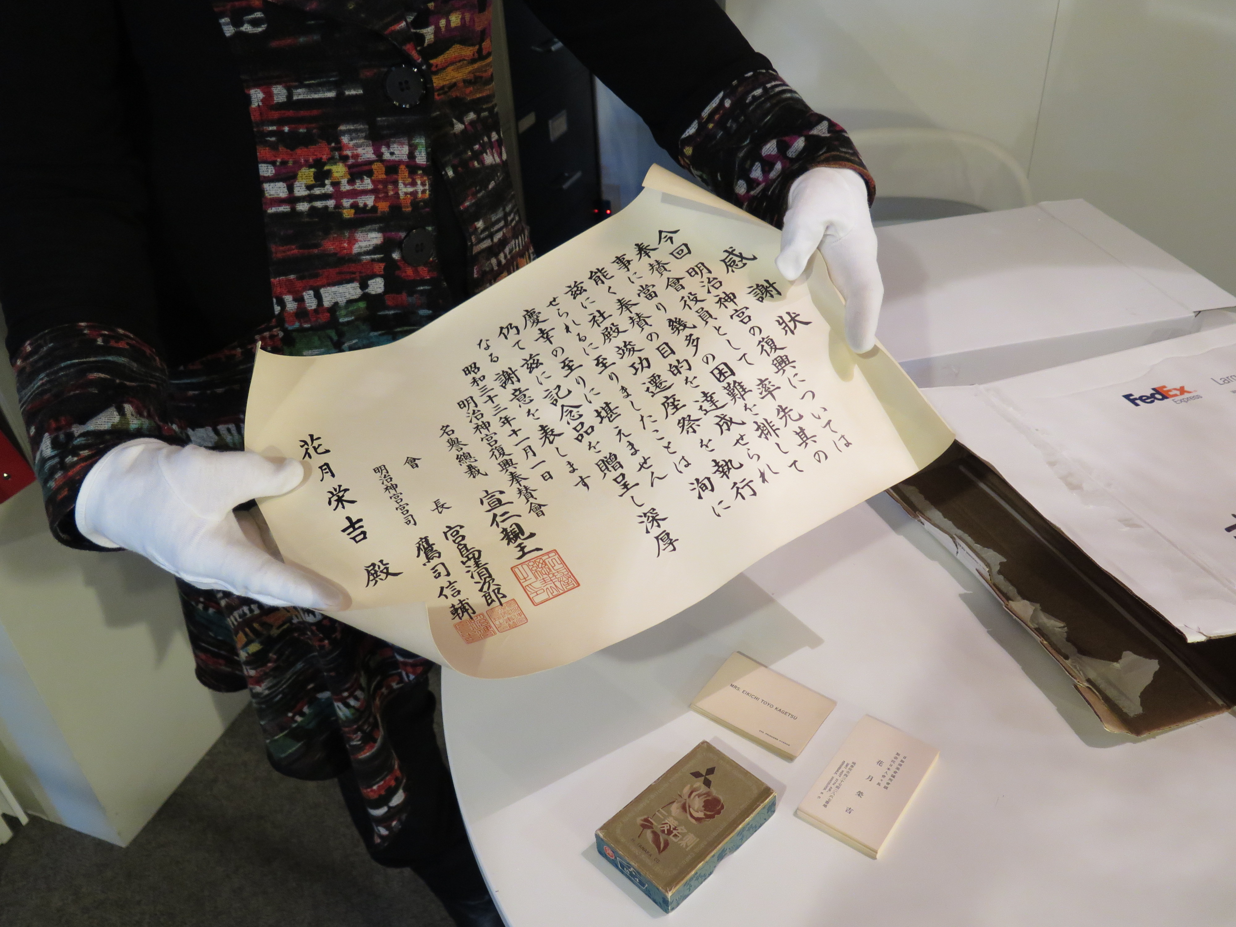 NNMCC Research Archivist Linda Kawamoto Reid displays a scroll after donning protective gloves to handle the historic material. At the time of this photo, the collection was in banker boxes bagged and ready to be placed in an off-site freezer to destroy any mold or insects that may have made its way into the material while it was stored in the Kagetsu family’s North Carolina basement. 