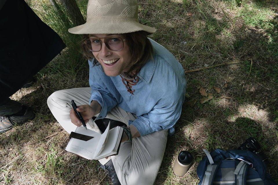 Graeme sitting on grass floor with a pen and notebook